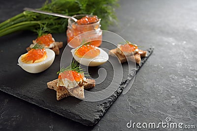 Red caviar on halved eggs and on toasted canapes in star shape with dill, preparation for a festive Christmas buffet on a dark Stock Photo