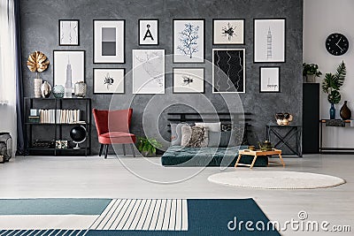 Red chair next to green futon with pillows in grey apartment interior with posters and rug. Real photo Stock Photo