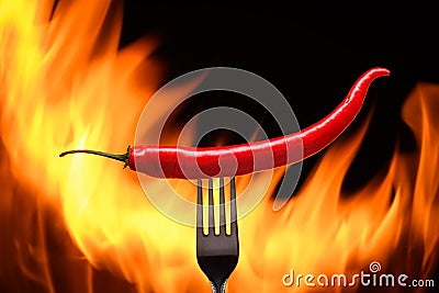 red chili pepper, pricked on a fork, on a background of burning fire, flames on a black background Stock Photo