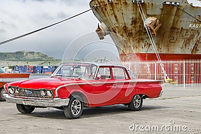 Red classic american car - Ford - in front of rusty ship in harbor of Santiago de Cuba Editorial Stock Photo