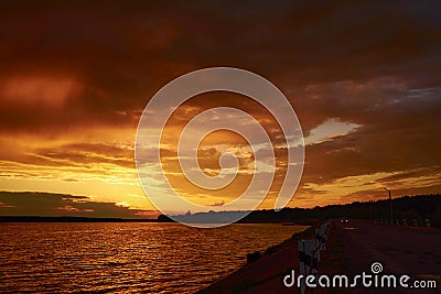 Fiery orange sunrise over river dam. Car on the road under clouds at dusk. Cloudscape in twilight. Bloody sky. Last day on Earth. Stock Photo