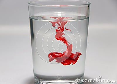 Red color drop on the water in the glass with white background. Stock Photo