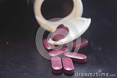 Red coloured pills spilling out of a pill bottle Stock Photo