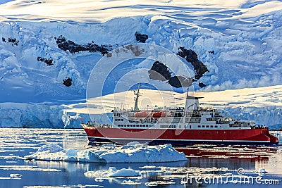 Red cruise steamboat among the icebergs with glacier in background, Neco bay, Antarctica Stock Photo