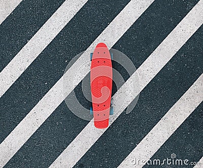 Red cruiser board on dark gray and white crosswalk. Plastic penny skateboard on asphalt, shot from the top. Stock Photo