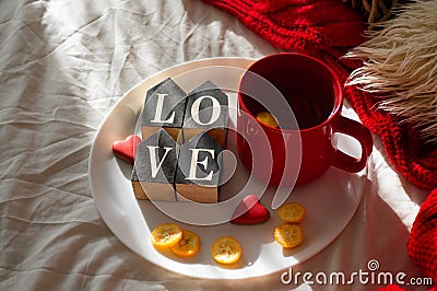Red cup of tea with kumquat on the plate and two hearts cookies with the word LOVE on a white bed. Valentines day concept. Stock Photo