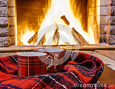 Red cups for hot tea and cozy warm scarf near fireplace. Stock Photo