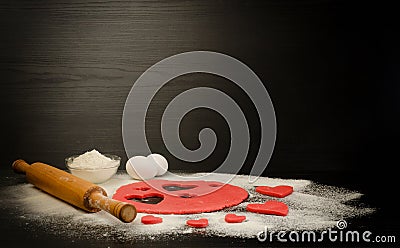 Red dough, cut out hearts, flour, eggs and rolling pin on a black background Stock Photo