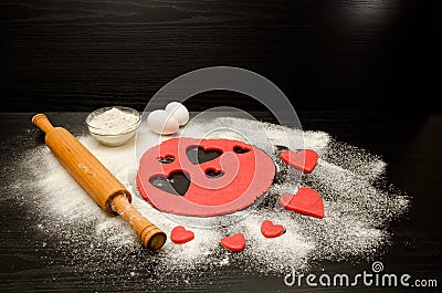 Red dough, cut out hearts, flour, eggs and rolling pin on a black background, space for text Stock Photo