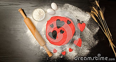 Red dough, cut out hearts, flour, eggs and rolling pin on a black background, space for text Stock Photo