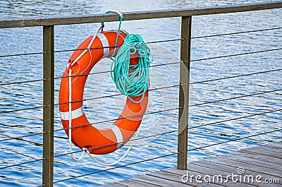 Red emergency lifebuoy with turquoise rope on pier near sea Stock Photo