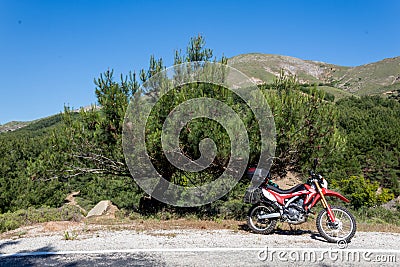 A red enduro motorcycle stands in side of the asphalt road, green nature Editorial Stock Photo