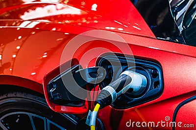 Red EV Car at charging station with the power cable supply plugged in. Power supply connect to electric vehicle for charging the Stock Photo