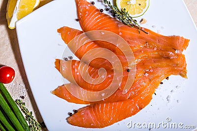 Red fish sliced in slices lies on a white plate. Around vegetables and slivers Stock Photo