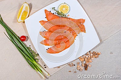 Red fish sliced in slices lies on a white plate. Around vegetables and slivers Stock Photo