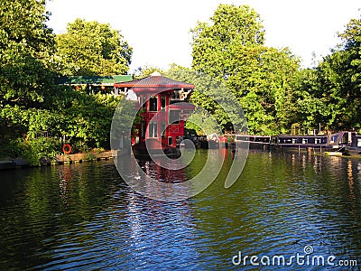 A red floating Chinese restaurant Feng Shang Princess hidden by the side of the Regent`s Canal in Camden Editorial Stock Photo