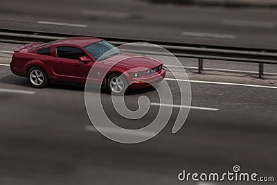 Red ford mustang rides on the road. Against a background of blurred trees Editorial Stock Photo