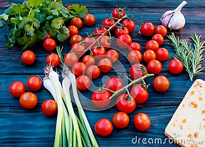 Red fresh tasty cherries, green spring onions, green rosemary, leaves of coriander, sweet cheese, garlic on dark wo Stock Photo