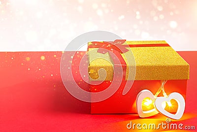 Red gift box with a bow and a heart with a glowing lamp inside on a red background with gold glitter, copyspace. Universal holiday Stock Photo