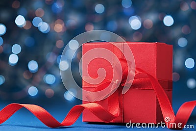 Red gift box or present with bow ribbon against blue bokeh background. Christmas greeting card. Stock Photo