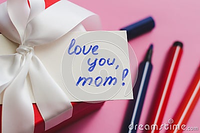 Red gift box tied with a white ribbon, markers and a card with an inscription on a pink background. Stock Photo