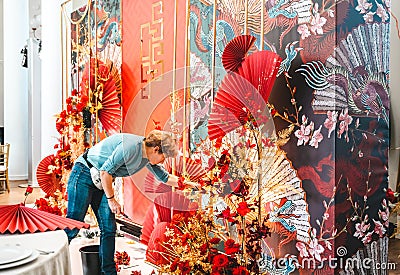 Red gold color flower decor for Chinese New Year celebration. Girl woman florist, decorator, organizer of events Editorial Stock Photo