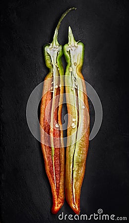 Red and green chilli pepper sliced lengthwise over a black slate . Stock Photo