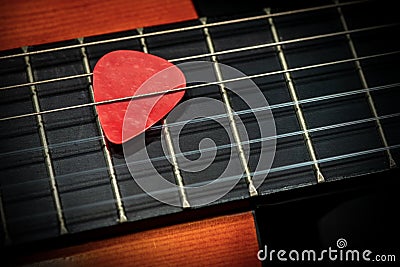 Red Guitar Pick Between the Strings of an Old Acoustic Guitar Stock Photo