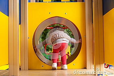 Red hair little girl crawling through the tunnel in the playground Stock Photo