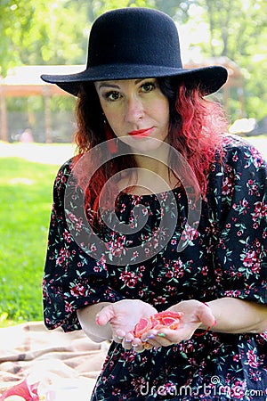 a red-haired, curly-haired woman in a black hat, a matching dress and red tasseled earrings holds view candy marmalade in her Stock Photo