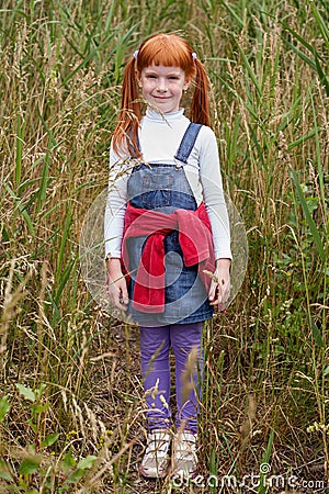 red-haired girl with freckles standing in tall grass Stock Photo