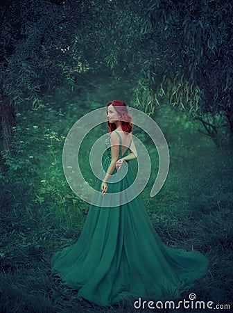 Red-haired girl in a green, emerald, luxurious dress in the floor, with an open back and a long train. The princess Stock Photo