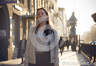 A red-haired girl walks along the sunlit street Stock Photo