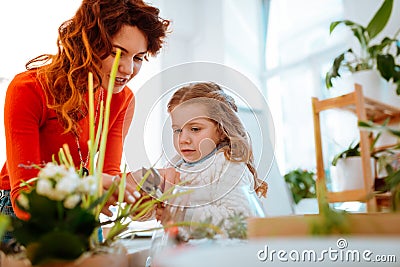 Red-haired mom cutting dry edges of home plant with daughter Stock Photo