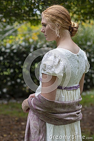 Regency woman in cream dress walks alone in a summer garden Stock Photo