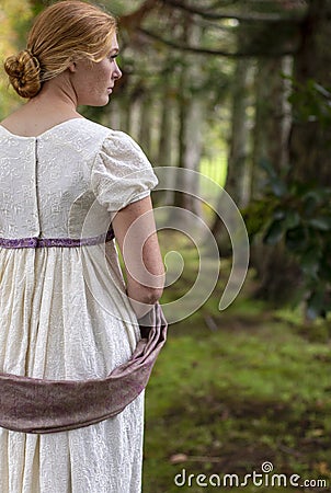 Regency woman in cream dress walks alone in a summer garden Stock Photo