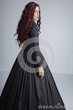 Red-haired woman in Black Victorian ensemble and a witch-like pose Stock Photo