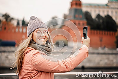 Red-haired woman in glasses traveler in a hat and jacket chatting on a smartphone taking a selfie in Moscow Stock Photo