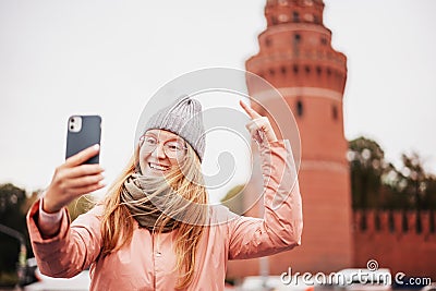 Red-haired woman in glasses traveler in a hat and jacket chatting on a smartphone while taking a selfie in Moscow, on Kremlin Stock Photo