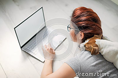 Red-haired woman in isolation lying on the floor with a dog. The girl maintains a social distance and works from home on Stock Photo