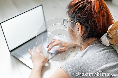 Red-haired woman in isolation lying on the floor with a dog. The girl maintains a social distance and works from home on Stock Photo