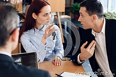 Red-haired woman is holding on finger keys sitting next to adult man in lawyer`s office. Stock Photo