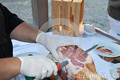 Red ham cut by hand chef professional cutter carving slices from whole bone in serrano ham Stock Photo