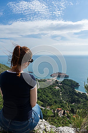 Red head girl hill enjoying Sveti Stefan island in Budva, Montenegro. Young woman looking to the adriatic sea and green cliff. Stock Photo