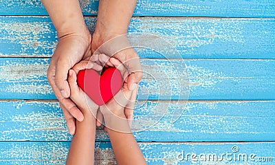 Red heart in child kid and mother hands on old blue wooden table Stock Photo