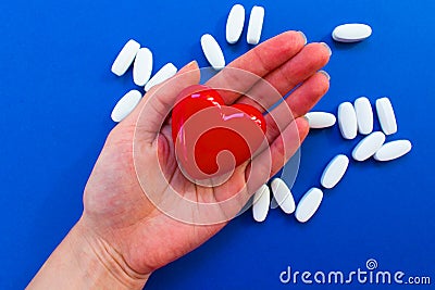 Red heart on the female palm on a blue background with white pills ... Stock Photo