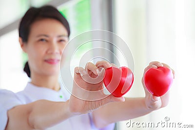 Red heart held by smiling female nurse`s hand, representing giving effort high quality service mind to patient. Professional Stock Photo