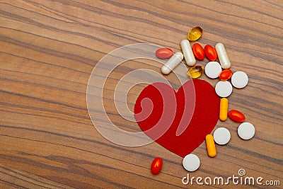 Red heart and many bright pills drugs on wooden background. Stock Photo