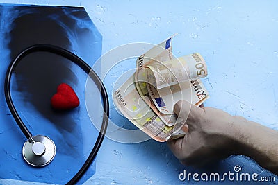 Red heart and phonendoscope near the radiograph of the lungs, chest of a patient with pneumonia. Money in a man`s hand. Corruptio Stock Photo