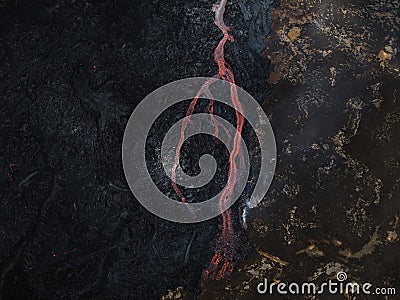 Red hot lava flow streaming over black volcanic rocks, aerial directly above Stock Photo